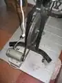 A fan belt is wrapped around the flywheel of an exercise bike and the pulley of high voltage, low rpm permanent magnet dc generator. 110v blenders and some other low power ac appliances can be powered provided they are built using universal motors which run on ac or dc. The next stage of development of this project is to mount the generator directly to the frame of the exercise bike via a gravity tensioned swing arm. This will eliminate the need for the heavy wooden pedistle upon which the generator is currently mounted. The electrical wiring should be brought up to code. Transparent lexan-polycarbonate finger gaurds should be installed to prevent children from catching their figures between the fanbelt, pulley and flywheel. Lastly, large caster wheels should then be mounted to the base of the exercise bike's frame so that the devise can be moved easily. Because of the redundant nature of an exercise bike as compared to a bicycle that is used for transportation, a system should be designed that incorporates a blender, powered by a generator mounted on a bicycle that tows an ice-box trailer.