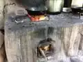 Wood is inserted into the chambers on the side of the stove. The flames rise through a chimney, and the heat escapes through the top opening, where it can be used to cook food.